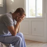 Man Wearing Pajamas Sitting On Bed With Head In Hands