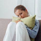 Sad depressed woman at home, she is sitting on the couch and hugging a pillow, loneliness and sadness concept